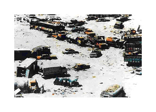 Photo of a chaos of broken-down vehicles in a parched white desert, most of them in two parallel lines as on a highway . There are all kinds of vehicles - mostly passenger cars and pickup trucks, a couple of buses, tanker trucks, cargo trucks; not a single military vehicle.